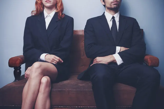 Two sharply dressed business people are waiting on a sofa with a serious expression on their faces. Maybe they're waiting to enter a job interview, or maybe they're a couple waitng to see a divorce lawyer. (Photo by Lofilolo/Getty Images/iStockphoto)