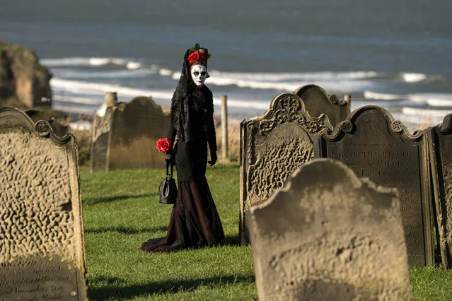 A participant in costume walks between the gravestones in St Mary's church graveyard beside the Abbey during the biannual “Whitby Goth Weekend” festival in Whitby, northern England, on October 27, 2019. The festival brings together thousands of goths and alternative lifestyle fans from the UK and around the world for a weekend of music, dancing and shopping. (Photo by Oli Scarff/AFP Photo)