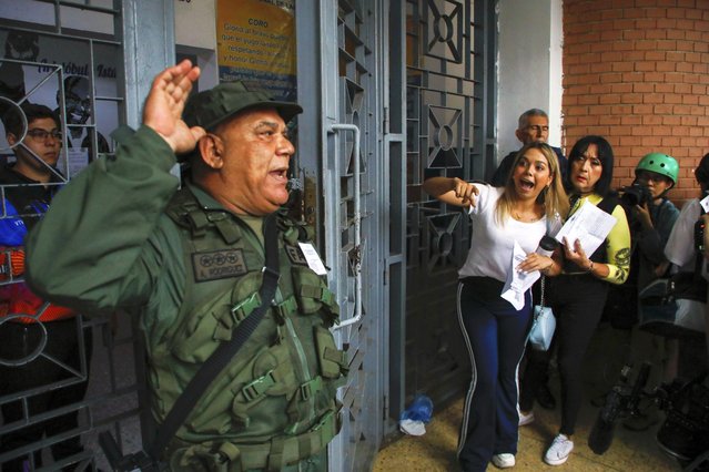 A National Guard officer addresses voters lining up at the Andres Bello School as opposition poll watchers argue they are not being allowed to enter the voting center during the presidential elections in Caracas, Venezuela, Sunday, July 28, 2024. (Photo by Cristian Hernandez/AP Photo)