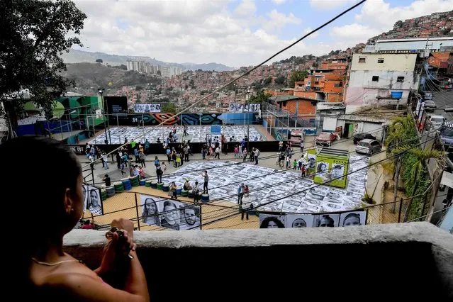 A woman looks as people place large-scale black and white portraits of members from the community of San Blas on display as part of the “Inside Out” global art project by French photographer JR, in the neighbourhood of Petare in Caracas, on April 12, 2022. (Photo by Federico Parra/AFP Photo)