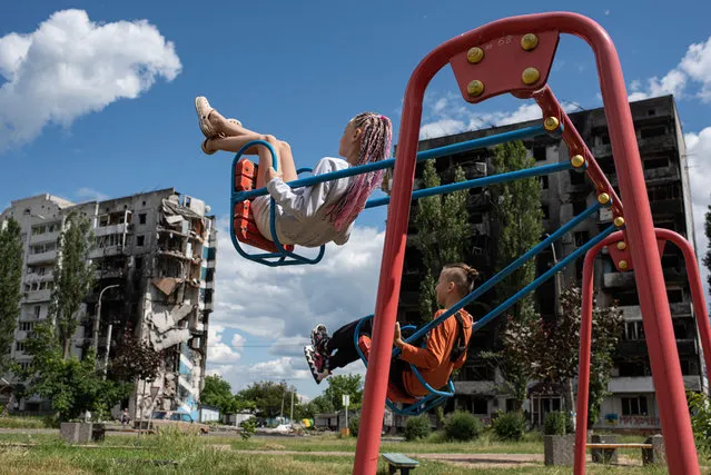 A girl and a boy swing on a swing next to a shelled apartment building on June 15, 2022 in Borodianka, Ukraine. The region around Ukraine's capital continues to recover from Russia's aborted assault on Kyiv, which turned many communities into battlefields. (Photo by Alexey Furman/Getty Images)