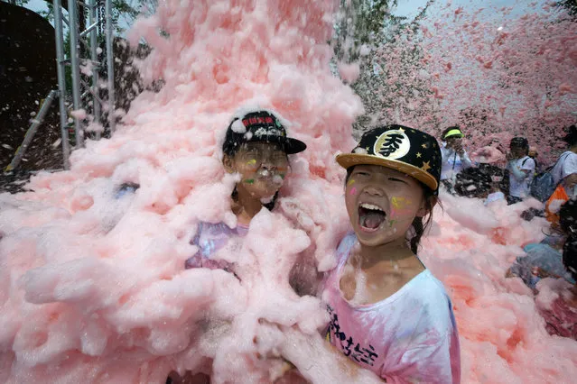 Children are engulfed by foam during the Bubble Show event in Beijing, China, Sunday, June 26, 2016. Thousands of residents enjoy colored foam churned out by machines along a running track at the event designed for children and parents'  interaction. (Photo by Ng Han Guan/AP Photo)
