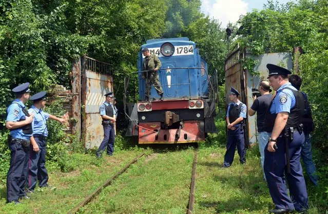 Police officers secure a refrigerated train loaded with bodies of the passengers of Malaysian Airlines flight MH17 as it arrives in a Kharkiv factory for a stop on Tuesday, July 22, 2014. The train carrying the remains of people killed in the Malaysia Airlines crash arrived in the eastern Ukrainian city of Kharkiv on Tuesday on their way to the Netherlands, a journey which has been agonizingly slow for relatives of the victims. (Photo by Genya Savilov/AFP Photo)