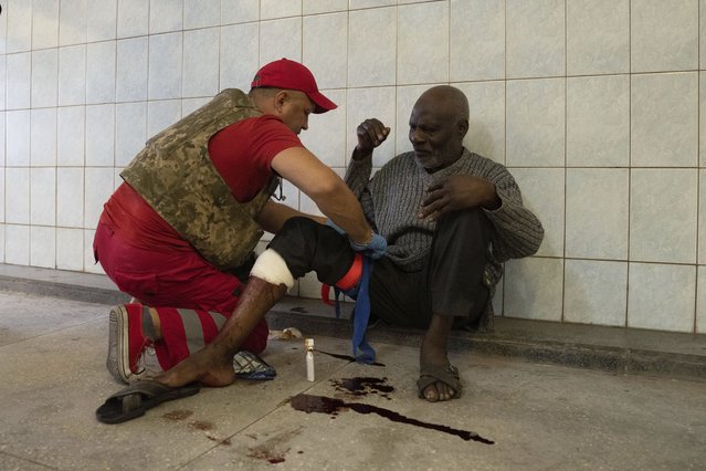 A medical worker treats an injured man after Russian shelling at Barabashovo market in Kharkiv, Ukraine, Thursday, July 21, 2022. (Photo by Evgeniy Maloletka/AP Photo)