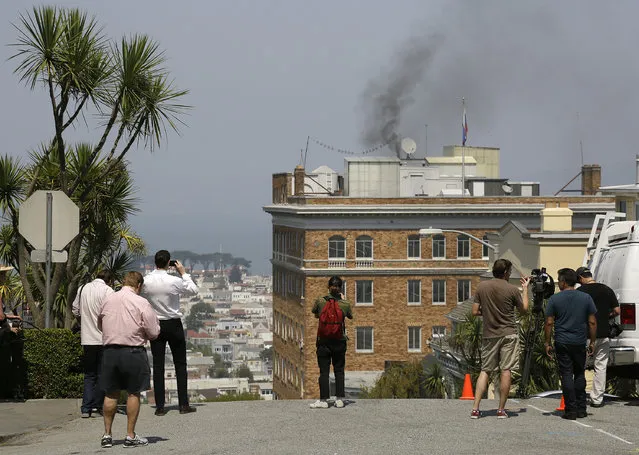 People stop to watch black smoke coming from the roof of the Consulate-General of Russia Friday, September 1, 2017, in San Francisco. The San Francisco Fire Department says acrid, black smoke seen pouring from a chimney at the Russian consulate in San Francisco was apparently from a fire burning in a fireplace. The smoke was seen billowing from the consulate building a day after the Trump administration ordered its closure. (Photo by Eric Risberg/AP Photo)