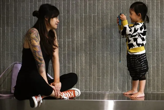 A visitor poses a photo for her daughter at the International Hong Kong China Tattoo Convention in Hong Kong August 22, 2014. The territory held its second international tattoo convention on Friday, hoping to pin Hong Kong onto the global tattoo-map and aiming at changing the perception of tattoos in a city where inked skin is still strongly associated with triads and criminals. (Photo by Bobby Yip/Reuters)