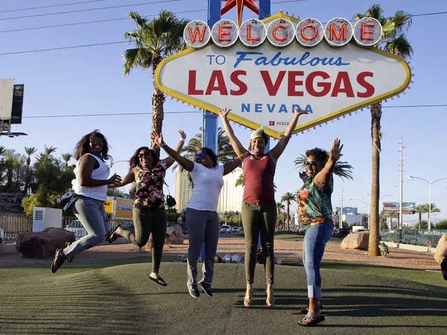 In this Tuesday, October 3, 2017 photo, tourists pose for photos in front of the Welcome to Las Vegas sign that has flowers honoring the people who died in a mass shooting on Sunday in Las Vegas. But even though the city is in mourning, for many it is business as usual with celebrations and parties continuing. (Photo by Chris Carlson/AP Photo)