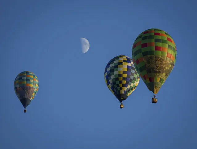 A trio of hot air balloons soar across the sky south of Indianola, Iowa, as the moon shines bright in the background during the National Balloon Classic, Friday, August 5, 2022. (Photo by Bryon Houlgrave/The Des Moines Register via AP Photo)