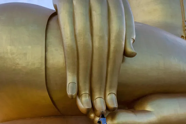 In this photo taken on July 2, 2020, a woman prays under the fingertips of the largest Buddha statue in Thailand, in Ang Thong province, north of Bangkok, as authorities reopened sites to tourists following lockdowns to halt the spread of the COVID-19 novel coronavirus. (Photo by Alex Ogle/AFP Photo)