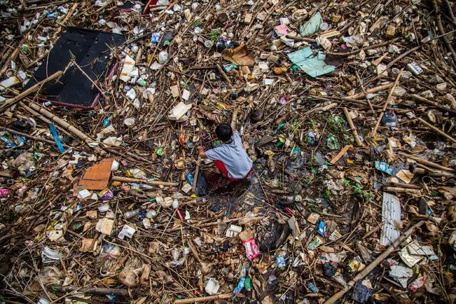 A boy plays on a drain covered with household waste in Bogor on December 16, 2022. (Photo by Aditya Aji/AFP Photo)