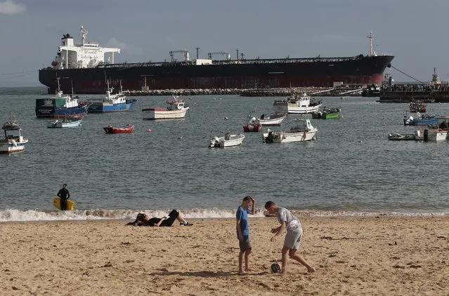 People play soccer and relax on the beach in front of empty oil tanker Tokyo Spirit, which ran aground on Saturday, next to a marina in the resort town of Cascais just outside Lisbon, Portugal, October 18, 2015. An operation is under way to free the Panama-registered Tokyo Spirit, which has 22 crew members onboard. (Photo by Hugo Correia/Reuters)