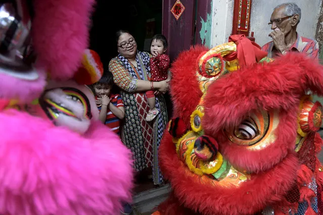 An Indian man, right, looks on as an ethnic Chinese woman and her children watch a lion dance procession on the first day of Chinese lunar new year in Kolkata, India, Friday, February 16, 2018. People in Asia and around the world are celebrating the Lunar New Year on Friday with festivals, parades and temple visits to ask for blessings. This year marks the year of the dog, one of the 12 animals in the Chinese astrological chart. (Photo by Bikas Das/AP Photo)