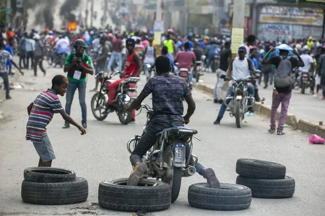 A motorcyclist uses his feet to drag tires into place for a barricade during a protest to demand the resignation of President Jovenel Moise in Port-au-Prince, Haiti, Saturday, October 17, 2020. (Photo by Dieu Nalio Chery/AP Photo)