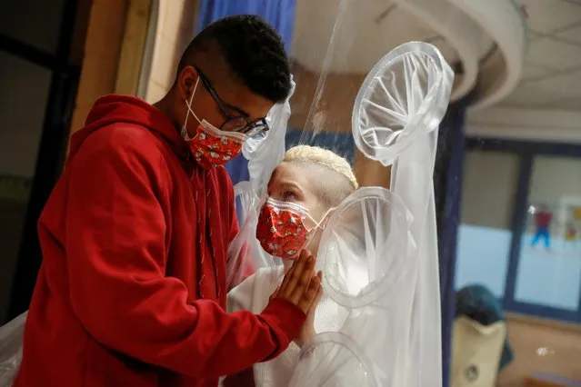 A hospitalized child meets his best friend through plastic at the Department of paediatric rehabilitation and developmental disabilities of IRCCS at the San Raffaele hospital, for children who wished for Christmas to see and hug their friends and family in Rome, Italy, December 22, 2020. (Photo by Yara Nardi/Reuters)
