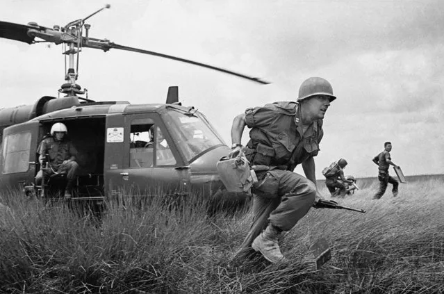 Capt. Donald R. Brown of Annapolis, Md., advisor to the 2nd Battalion of the 46th Vietnamese regiment, dashes from his helicopter to the cover of a rice paddy dike during an attack on Viet Cong in an area 15 miles west of Saigon on April 4, 1965 during the Vietnam War.  Brown's counterpart, Capt. Di, commander of the unit, rushes away in background with his radioman.  The Vietnamese suffered 12 casualties before the field was taken. (Photo by Horst Faas/AP Photo)