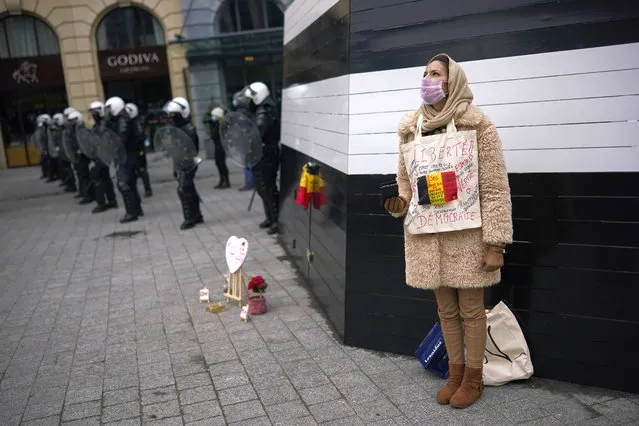 A woman, with the Belgium flag and a sign in French reading: “Freedom. Democracy” on her chest, stands next to anti riot police during an unauthorised demonstration against COVID-19 restrictive measures in Brussels, Sunday, January 31, 2021. According to Belgian media around 200 people have been arrested for trying to join a protest against restrictive measures implemented in the country in order to fight the virus, such as a 10pm curfew or the closing of bars and restaurants. (Photo by Francisco Seco/AP Photo)