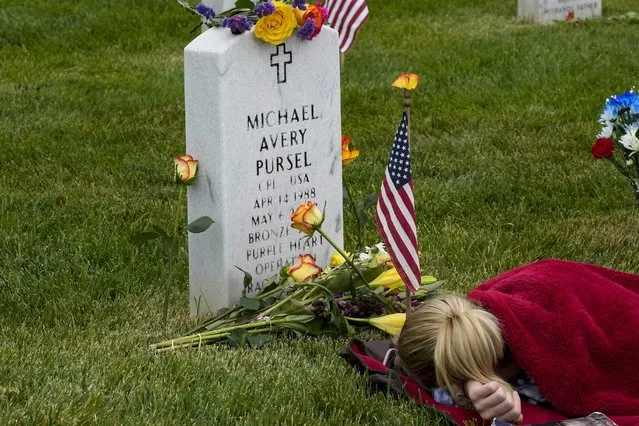 Avery Carlin, of Arlington, Va., rests by the headstone of her uncle U.S. Army Cpl. Michael Avery Pursel as she visits Section 60 at Arlington National Cemetery with her family on Memorial Day, Monday, May 29, 2023, in Arlington, Va. (Photo by Alex Brandon/AP Photo)