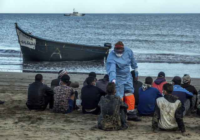 Migrants from Morocco have their temperature checked because of the coronavirus, after arriving at the coast of the Canary Island, crossing the Atlantic Ocean sailing on a wooden boat on Tuesday, October 20, 2020. Some 1,000 migrants have spent the night again sleeping in emergency tents in a dock while authorities in the Canary Islands complain that the Spanish government keeps blocking transfers of newly arrived migrants to the mainland over coronavirus concerns. (Photo by Javier Bauluz/AP Photo)
