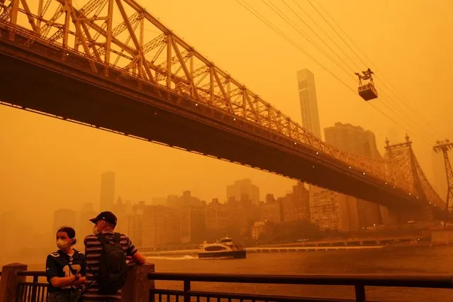 People wear protective masks as the Roosevelt Island Tram crosses the East River while haze and smoke from the Canadian wildfires shroud the Manhattan skyline in the Queens Borough New York City, U.S., June 7, 2023. (Photo by Shannon Stapleton/Reuters)