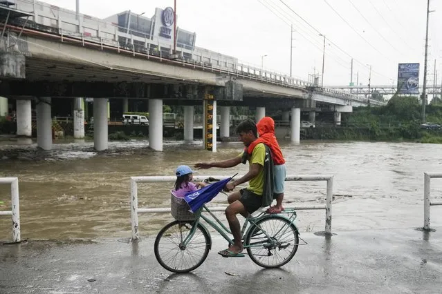 A man and children ride a bicycle beside a swollen river due to enhanced rains brought about by Typhoon Doksuri on Thursday, July 27, 2023, in Marikina city, Philippines. Typhoon Doksuri lashed northern Philippine provinces with ferocious wind and rain Wednesday, leaving several people dead and displacing thousands of others as it blew roofs off houses, flooded low-lying villages and triggered dozens of landslides, officials said. (Photo by Aaron Favila/AP Photo)