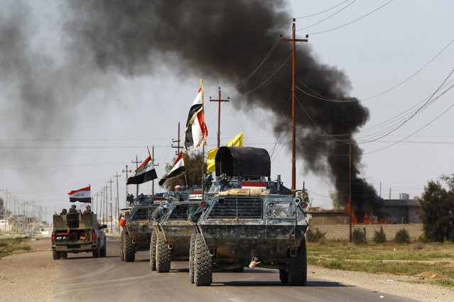 Armored vehicles of Iraqi security forces with militias known as Hashid Shaabi are driven past smoke arising from a clash with Islamic State militants in the town of al-Alam March 10, 2015. (Photo by Thaier Al-Sudani/Reuters)