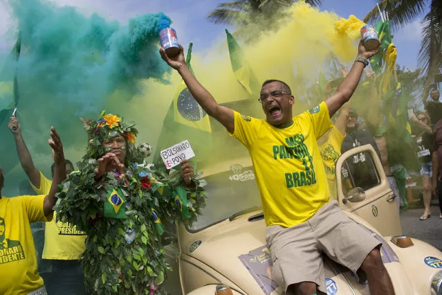 Supporters of presidential front-runner Jair Bolsonaro sing the national anthem outside his residence in Rio de Janeiro, Brazil, Sunday, October 28, 2018, during the country's presidential runoff election. Brazilian voters decide who will next lead the world's fifth-largest country, the left-leaning Fernando Haddad of the Workers' Party, or far-right rival Jair Bolsonaro of the Social Liberal Party. (Photo by Silvia Izquierdo/AP Photo)