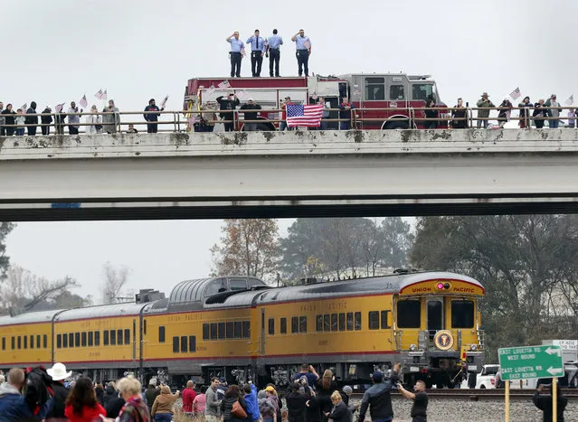 Firefighters stand on their truck and salute along with other attendants on an overpass as the train carrying the body of former president George H.W. Bush travels past on the way to Bush's final internment Thursday, December 6, 2018, in Spring, Texas. (Photo by Michael Wyke/AP Photo)