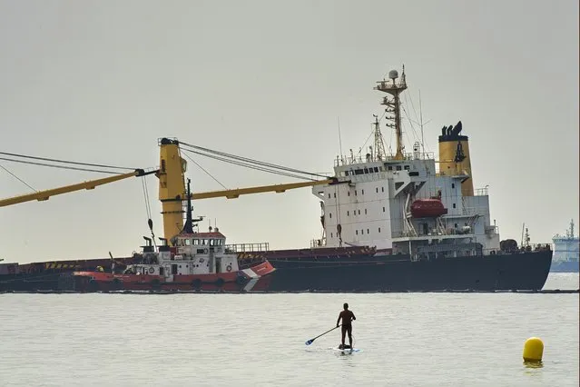 A man approaches with his paddle surf board to get a closer look at the Tuvalu-registered OS 35 cargo ship lying on the seabed, offshore Gibraltar, Tuesday, 30 August 2022. Gibraltar authorities say they have beached a cargo ship to prevent it from sinking after it collided with a liquid natural gas carrier early Tuesday in the bay of Gibraltar. (Photo by Marcos Moreno/AP Photo)