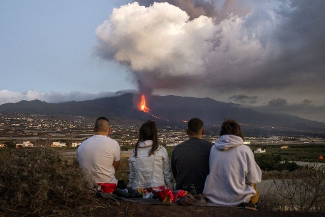 Residents watch as lava flows from a volcano as it continues to erupt on the Canary island of La Palma, Spain, Tuesday, October 26, 2021. Officials say a volcano erupting for the past five weeks on the Spanish island of La Palma is more active than ever. New lava flows have emerged following a partial collapse of the crater and threaten to engulf previously unaffected areas. (Photo by Emilio Morenatti/AP Photo)