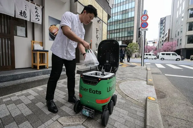 A restaurant employee places a food order inside an unmanned robot during a demonstration of a robot delivery service by Uber Eats Japan, Mitsubishi Electric and robot developer Cartken in downtown Tokyo on March 5, 2024. (Photo by Richard A. Brooks/AFP Photo)