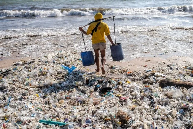 A man carrying buckets walks along a beach littered with piles of debris and plastic waste at the Kedonganan beach in Bali, Indonesia, 19 March 2024. Most of the trash ends up in the sea every rainy season due to the island's lack of a centralized waste management system. (Photo by Made Nagi/EPA/EFE)