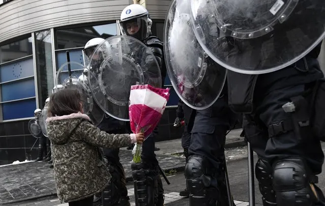 A girl gives flowers to riot police officers during a protest against coronavirus measures in Brussels, Belgium, Sunday, December 5, 2021. Hundreds of people marched through central Brussels on Sunday to protest tightened COVID-19 restrictions imposed by the Belgian government to counter the latest spike in coronavirus cases. (Photo by Geert Vanden Wijngaert/AP Photo)