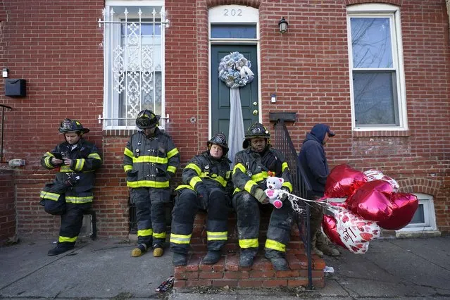 A Baltimore firefighter holds balloons given to him by neighbor Darlene Cucina as a group of fire officials sit on a stoop across the street where three firefighters died in a building collapse while battling a two-alarm blaze in a vacant row home, Monday, January 24, 2022, in Baltimore. Officials said a fourth firefighter is currently on life support at a local hospital. (Photo by Julio Cortez/AP Photo)