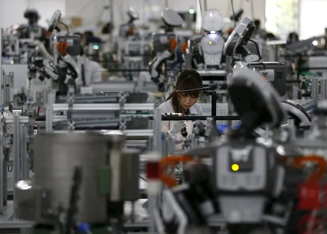 A humanoid robot works side by side with employees in the assembly line at a factory of Glory Ltd., a manufacturer of automatic change dispensers, in Kazo, north of Tokyo, Japan, July 1, 2015. (Photo by Issei Kato/Reuters)