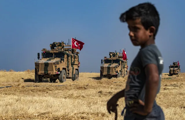 A Syrian boy watches as Turkish military vehicles, part of a US military convoy, take part in joint patrol in the Syrian village of al-Hashisha on the outskirts of Tal Abyad town along the border with Turkey, on October 4, 2019. The United States and Turkey began joint patrols in northeastern Syria aimed at easing tensions between Ankara and US-backed Kurdish forces. (Photo by Delil Souleiman/AFP Photo)