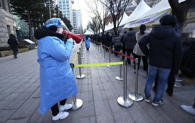 A medical worker uses a loud speaker to give information to people waiting for their coronavirus test at a makeshift testing site in Seoul, South Korea, Wednesday, February 23, 2022. South Korean health officials on Wednesday approved Pfizer’s coronavirus vaccine for the country’s unvaccinated younger children, expanding its immunization program in the face of a massive omicron outbreak that is beginning to drive up hospitalizations and deaths. (Photo by Ahn Young-joon/AP Photo)