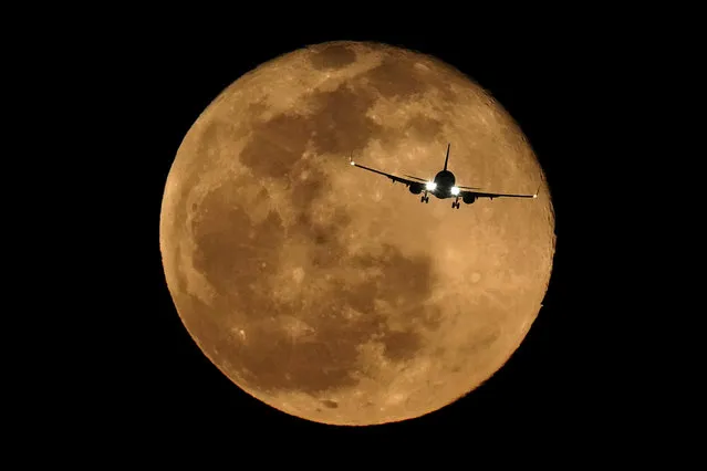 A passenger jet is silhouetted against the rising full moon on approach to Phoenix Sky Harbor International Airport, Friday, March 18, 2022, in Phoenix. (Photo by Charlie Riedel/AP Photo)