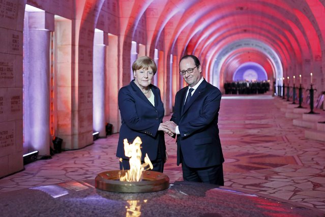 French President Francois Hollande and German Chancellor Angela Merkel stand hand in hand after lighting the eternal flame at Douaumont Necropolis and Ossuary, France, May 29, 2016, during a ceremony marking the 100th anniversary of the battle of Verdun, one of the largest battles of the First World War (WWI) on the Western Front. (Photo by Mathieu Cugnot/Reuters)