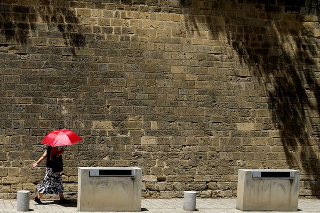 A woman protects her self from the sun with an umbrella as she's walks at Paphos gate at medieval core in central capital Nicosia, Cyprus, on Friday, June 14, 2024. The Meteorological Department said the heatwave's highest temperatures in this days they're expected to reach 45,3 degrees Celsius (113,54 Fahrenheit) inland and 35 degrees (95 Fahrenheit) in the island's main Troodos mountain range. (Photo by Petros Karadjias/AP Photo)