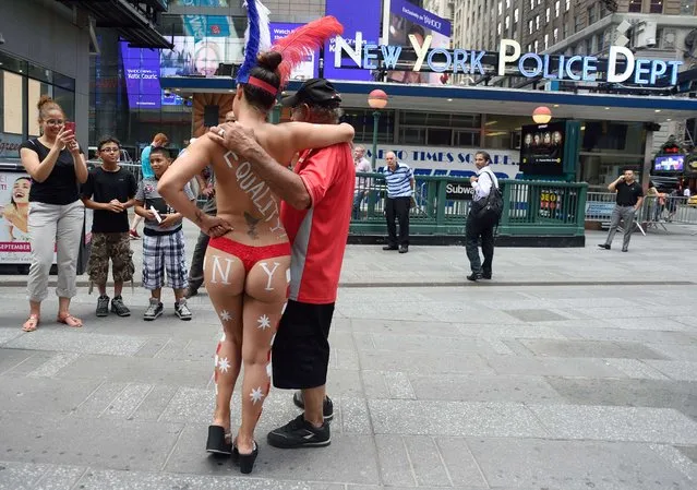 A young woman poses with tourists in Times Square wearing body paint to cover herself August 19, 2015 in New York. (Photo by Don Emmert/AFP Photo)