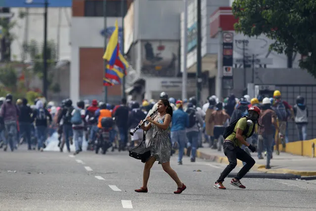 A young woman plays her clarinet in the midst of clashes between anti-government demonstrators and security forces, during a protest in Caracas, Venezuela, Thursday, July 6, 2017. The demonstrators were marching towards the Supreme Court when they were intercepted by authorities. Opposition protests demanding new elections and decrying triple-digit inflation, food shortages and worsening crime continue as President Nicolas Maduro pushes forward with his plan to draft a new constitution. (Photo by Ariana Cubillos/AP Photo)