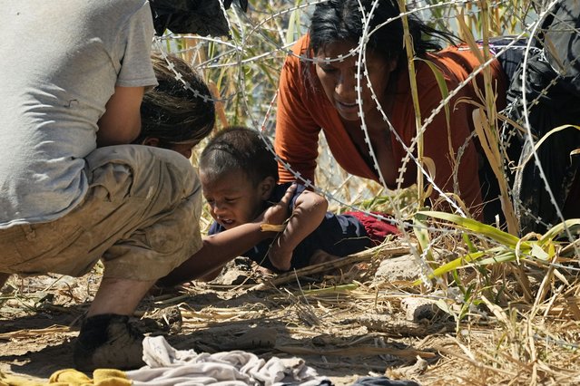 Migrants who crossed into the U.S. from Mexico pass under concertina wire along the Rio Grande river, Thursday, September 21, 2023, in Eagle Pass, Texas. (Photo by Eric Gay/AP Photo)