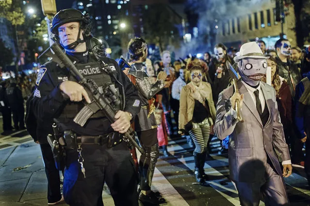 Heavily armed police guard as revelers march during the Greenwich Village Halloween Parade, Tuesday, October 31, 2017, in New York. New York City's always-surreal Halloween parade marched on Tuesday evening under the shadow of real fear, hours after a truck attack killed several people on a busy city bike path in what authorities called an act of terror. (Photo by Andres Kudacki/AP Photo)
