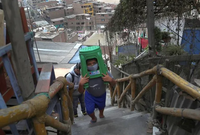 Twelve-year-old Yacdel Flores, hauling hard plastic stools, ascends a flight of stairs to the top of a hill to receive a free haircut from 21-year-old barber Josue Yacahuanca, in the San Juan de Lurigancho neighborhood of Lima, Peru, Friday, June 19, 2020. There are around 150,000 hairdressers in Peru, but Yacahuanca is one of the few who decided to offer his services for free to those most in need amid the new coronavirus pandemic. (Photo by Martin Mejia/AP Photo)