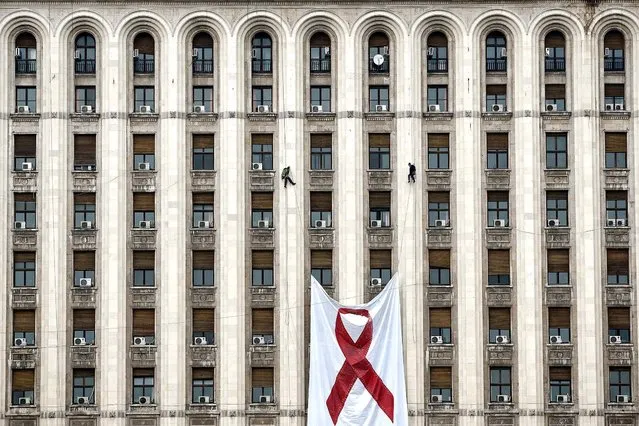 Workers lift a large AIDS awareness banner on the facade of a communist era building – a replica of the Lomonosov Moscow State University – now hosting the offices of some of the leading Romanian newspapers, in Bucharest, November 25, 2012. According to non-governmental organizations, more than 10,000 people live with AIDS in Romania but the actual number could be much higher as testing for the infection is not popular among Romanians. (Photo by Vadim Ghirda/Associated Press)