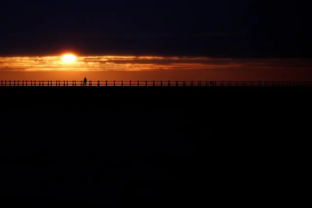 People look on as the sun rises during Summer Solstice, as seen from Roker Beach in Sunderland, Britain on June 21, 2020. (Photo by Lee Smith/Reuters)