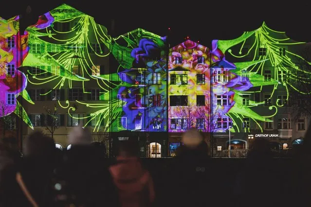 People watch at the facades of houses at Mariahilf illuminated to celebrate the New Year 2023 in Innsbruck, Austria, on December 31, 2022. (Photo by JFK via AFP Photo)