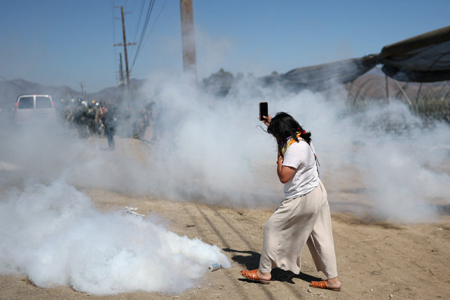 A woman holds a cellphone and covers her face as U.S. federal agents use tear gas while blocking a road leading to an agricultural facility where U.S. federal agents and immigration officers conducted an operation, in Camarillo, California, on July 10, 2025. (Photo by Daniel Cole/Reuters)