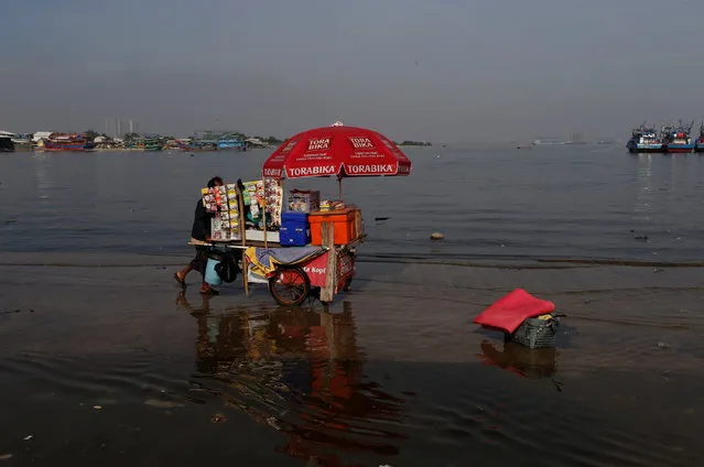 A street vendor pushes a food cart as sea water rises during high tide at the pier of Kali Adem port in Jakarta, Indonesia, January 3, 2018. (Photo by Reuters/Beawiharta)