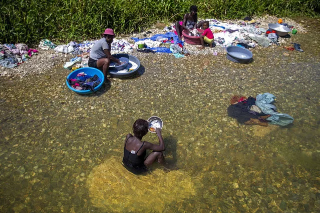 Geraldine Pierre 14, front, eats as she takes a break from washing clothes with her family in the Meille River near a former UN base in Mirebalais, Haiti, Monday, October 19, 2020. Ten years after a cholera epidemic swept through Haiti and killed thousands, families of victims still struggle financially and await compensation from the United Nations as many continue to drink from and bathe in a river that became ground zero for the waterborne disease. (Photo by Dieu Nalio Chery/AP Photo)